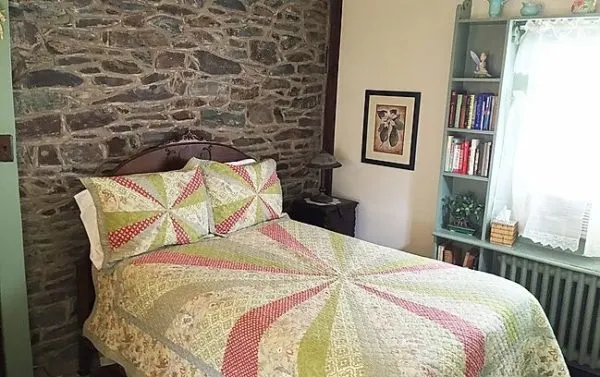 one of the cozy rooms at the lgbt-friendly wishing well b&b in new hope, pa has a retro bed spread, stone wall and pale turquoise trim.