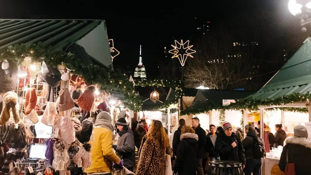 My 11 Absolute Favorite Nyc Christmas Things To Do With Kids the holiday market at nyc's union market at night with empire state building behind it.