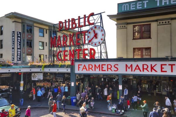 the clock, neon sign and busy stalls of pike place public market in downtown seattle.