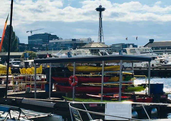 A stack of kayaks on lake union in seattle with the space needle in the background.