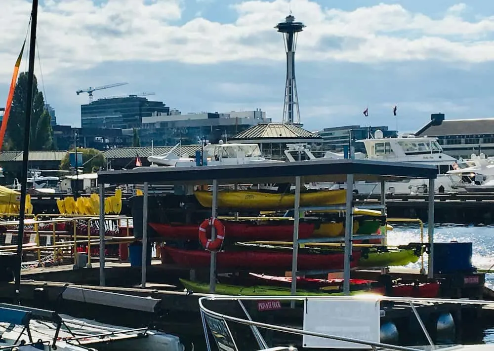 a stack of kayaks on lake union in seattle with the space needle in the background.