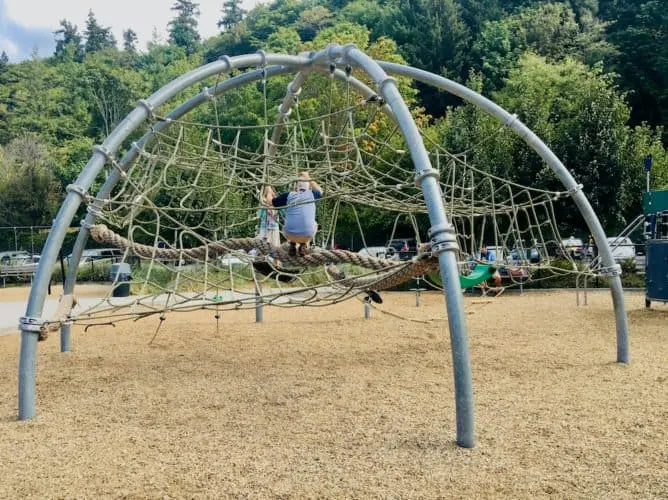 a dad and daughter climb the giant web at golden gardens park in seattle.