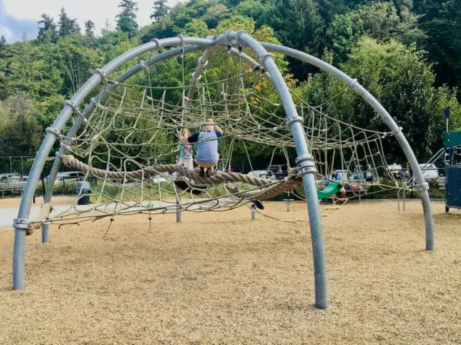 Seattle Weekend Getaway: 15 Of The Best Things To Do With Kids a dad and daughter climb the giant web at golden gardens park in seattle.