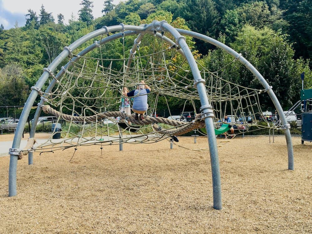 A dad and daughter climb the giant web at golden gardens park in seattle.