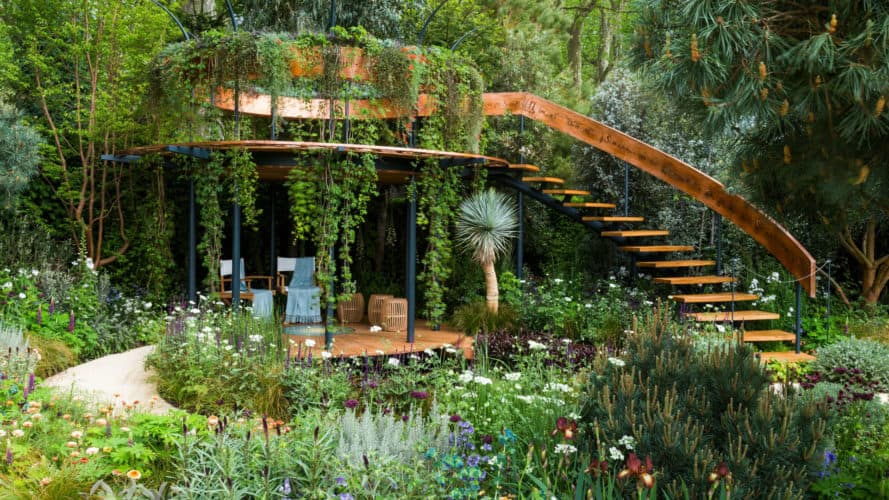 A lush, green outdoor living room with stairs, a balcony and a sitting area, at the chelsea flower show