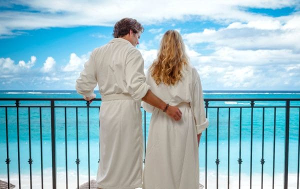 A couple in bathrooms admire the caribbean sea from their balcony during a familymoon moment without the kids.