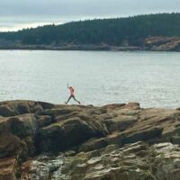 A girl jumps along boulders on the coast of Acadia National Park