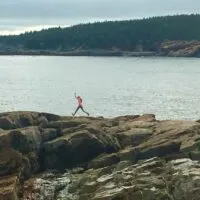 A girl jumps along boulders on the coast of Acadia National Park