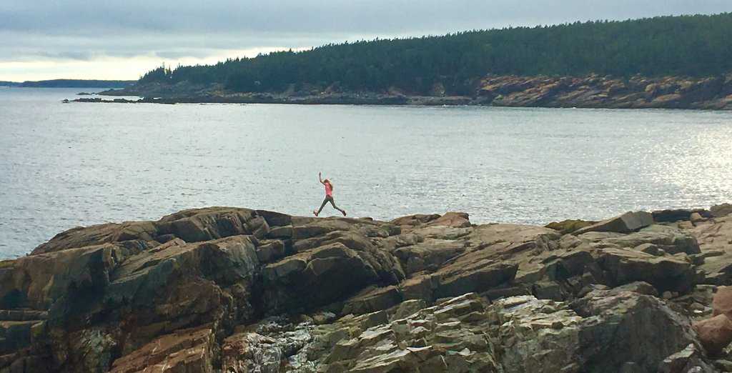 A girl jumps along boulders on the coast of Acadia National Park