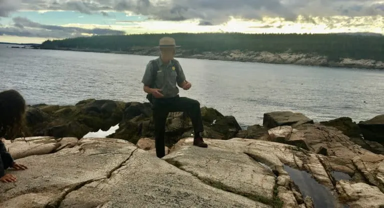 a national park ranger explains acadia's geology from atop some of its coastal boulders.