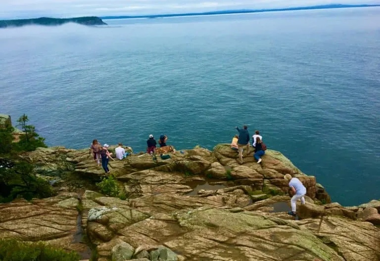 people exploring the tide pools and admiring the harbor view from acadia's rocky shore line.