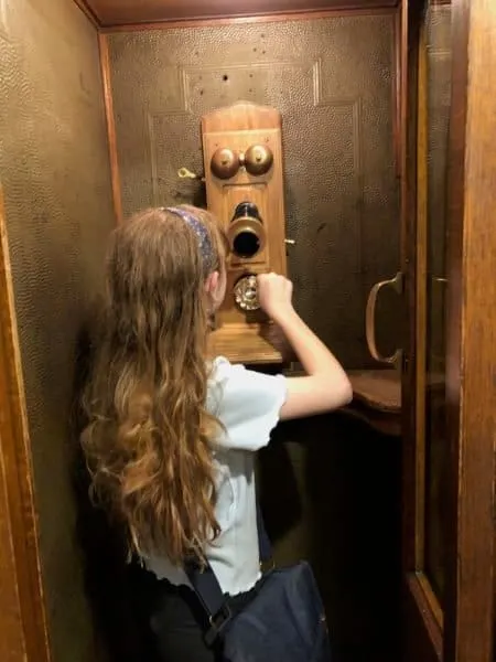 a girl pretends to dial an early 20th century phone in a phone booth  at the green mountain inn.