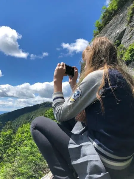 a teen girls takes photos of thew view from a stop on the cliffside trail in mansfield state forest in vermont.