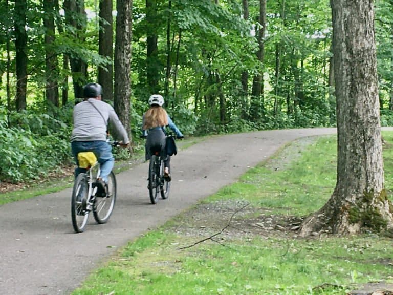 A dad & daughter bike along a woodsy stretch of the stowe recreation path.