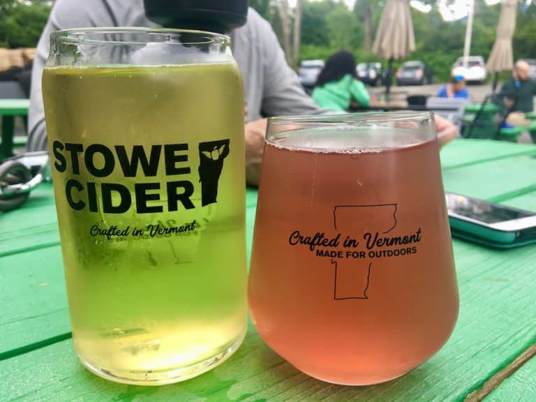 Two glasses of stowe cider, one pink from added berries, on a picnic table in their outdoor tasting space.