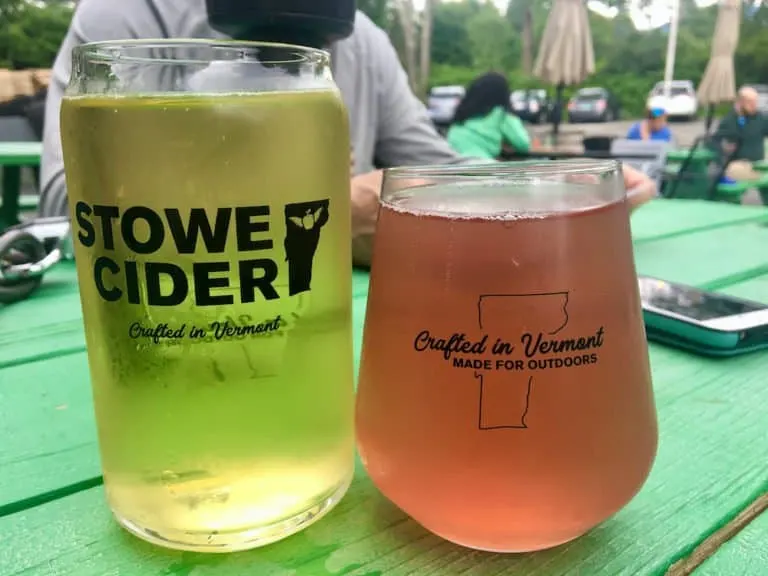 two glasses of stowe cider, one pink from added berries, on a picnic table in their outdoor tasting space.