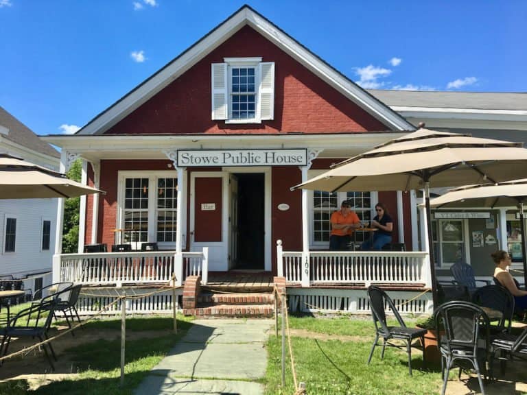 the stowe public house is an old new england house with a porch and outdoor seating right on main street.