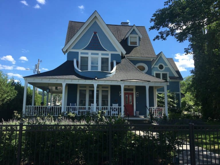 A blue victorian house with a porch and a hodge podge of peaks and windows in downtwon stowe.