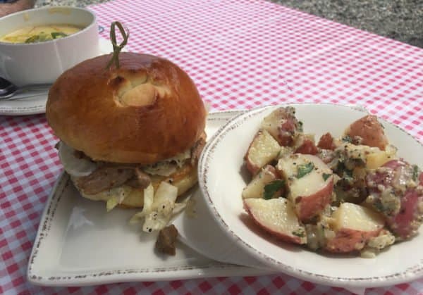 Cheese soup, a pork sandwich and austrian potato salad on a checkered table cloth typical of an austrian bier garten at the von trapp bierhall in stowe.