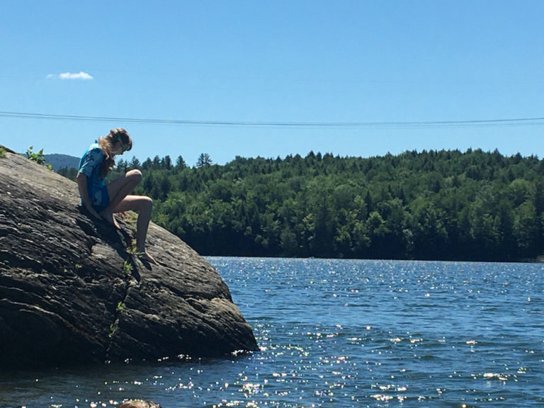 a girl sits on a giant boulder getting ready to jump into the waterbuty reservoir