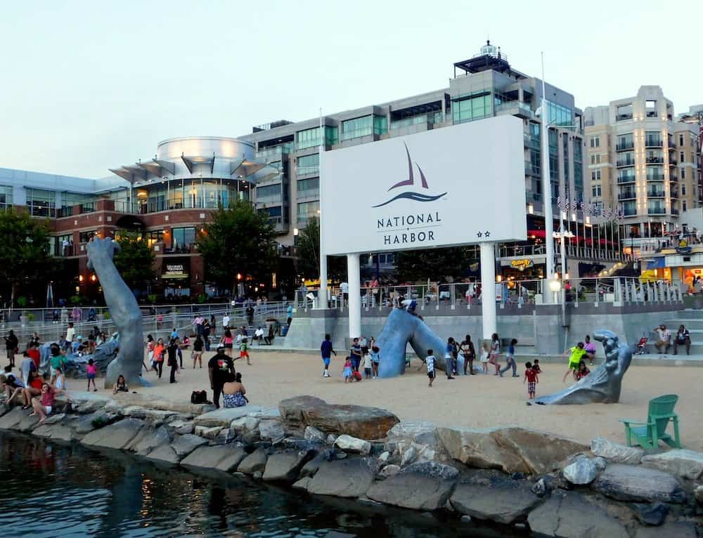 Kids climb on pieces of the awakening on the beach at national harbor, an easy weekend getaway from washington, dc. Hotels and shops are in the background.