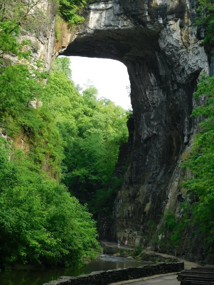 natural bridge state park in virginia is stunning with its towering stone arch. two tiny people stand beneath it to show the scale.