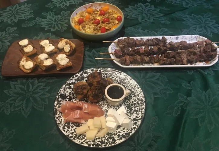4 plates of cicchetti for an italian night tapas party: beef skewers, onion-jam bruscetta, an antipasti plate with balsamic vinegar adnd raviolio with a cheese pesto.