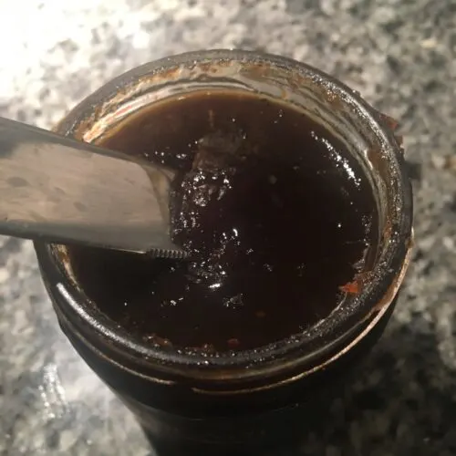 scooping onion jam from a jar with a knife for the base of our easy bruschetta