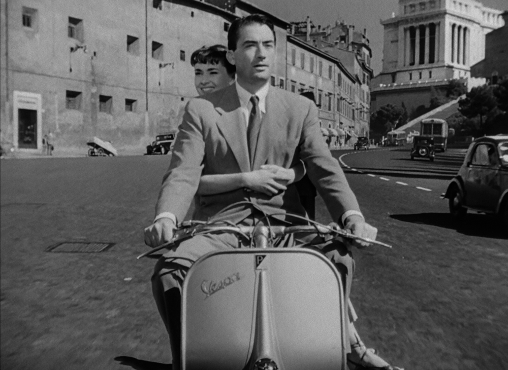 audrey hepburn and gregory peck ride a vespa through rome in roman holiday, the best movie for a staycation italian night movie party.