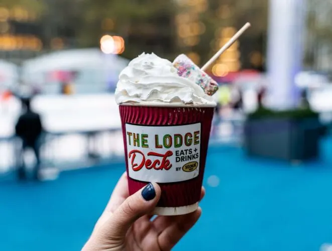 fancy hot chocolate with whipped cream and a giant, rainbow marshmallow on a stick, available at the lodge deck at bryant park winter village. 