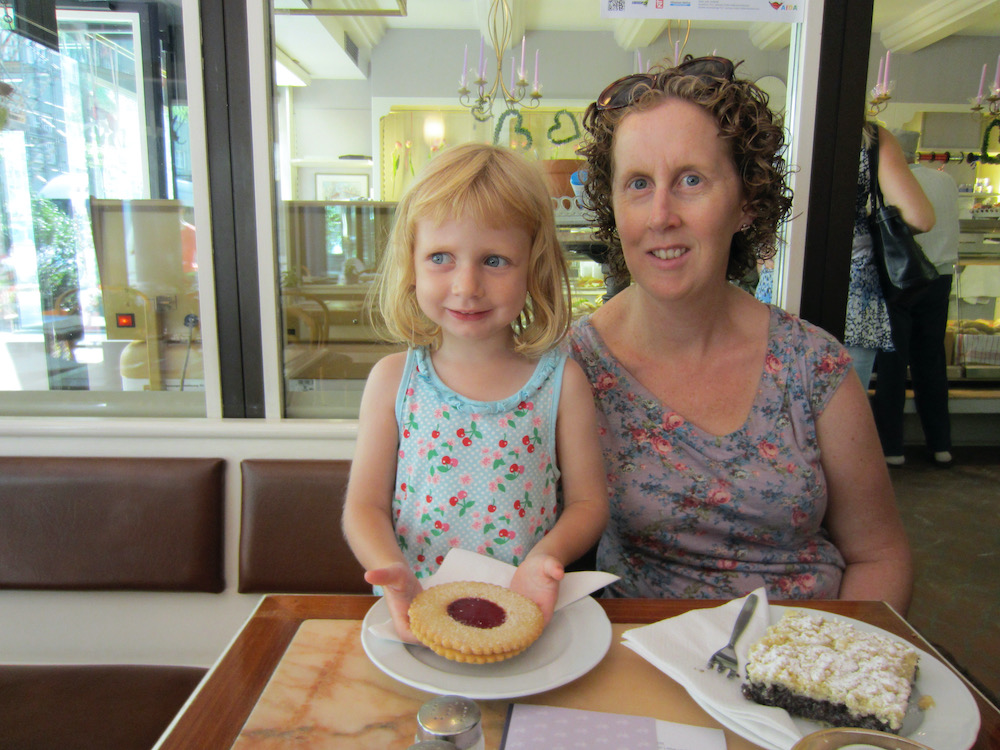 a mom has a slice of poppy seed cake and a little girl has a linzer torte cookie at a bakery in munich.