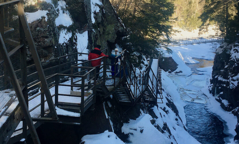 a dad and daughter walk along the suspended walks above the frozen rivers and waterfalls of high falls gorge in the adirondacks.