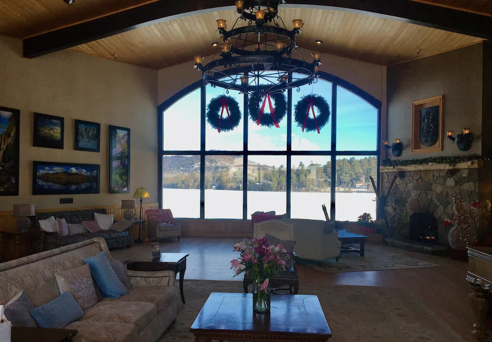 the lobby of the golden arrow hotel has a fireplace and glass wall with a view over mirror lake.