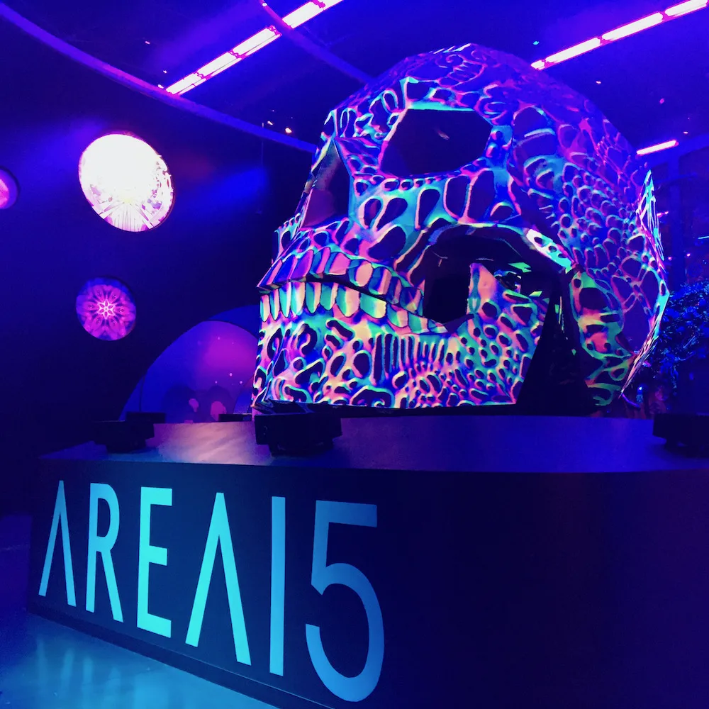 a large neon skull in a black-lit mall greets you as you enter area 15 in las vegas