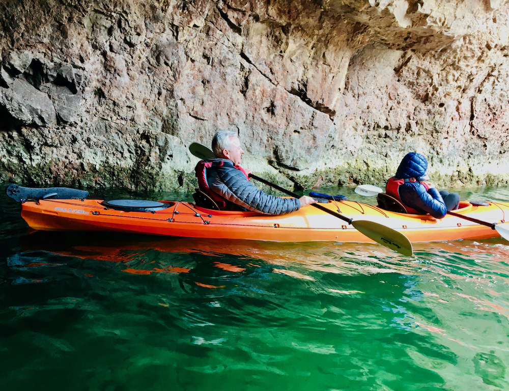A dad and daughter rest in their kayak in nevada's emerald cave with its jewel-colored water.