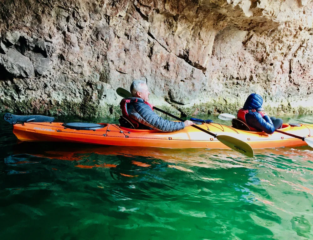 a dad and daughter rest in their kayak in nevada's emerald cave with its jewel-colored water.