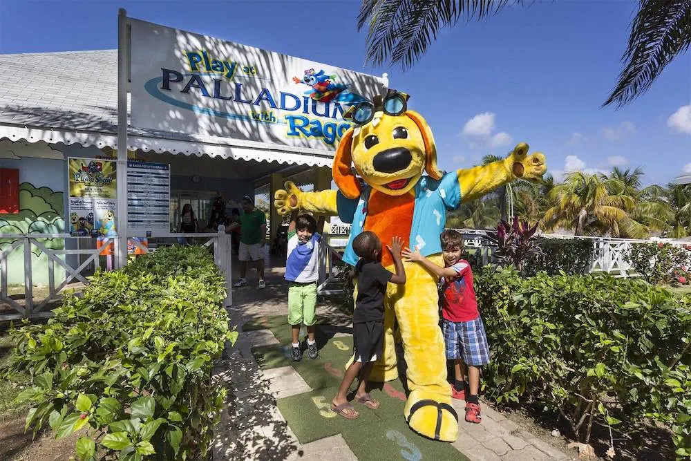 an interracial group of kids hugs raggs, yellow dog that is the mascot for divi resorts, a family friendly brand that is priced fairly for single parents.