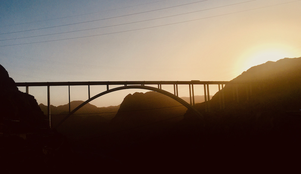 The sun going down behinnd the hoover dam memorial bridge that connects arizona and nevads