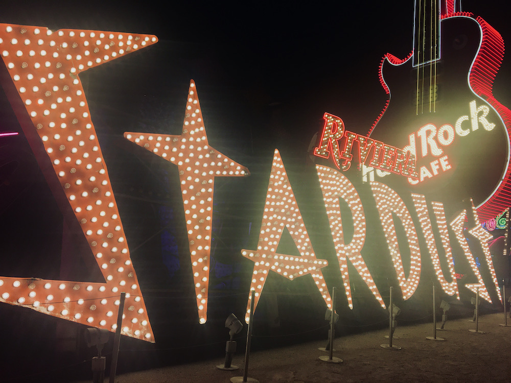 A collection of neon las vegas hotel signs including the stardust and a hard rock guitar, at the boneyard of the neon museum