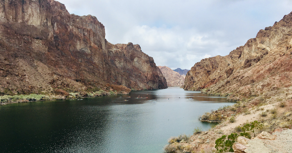 a view of kayakers making their way down the colorado river between rusty mountain walls