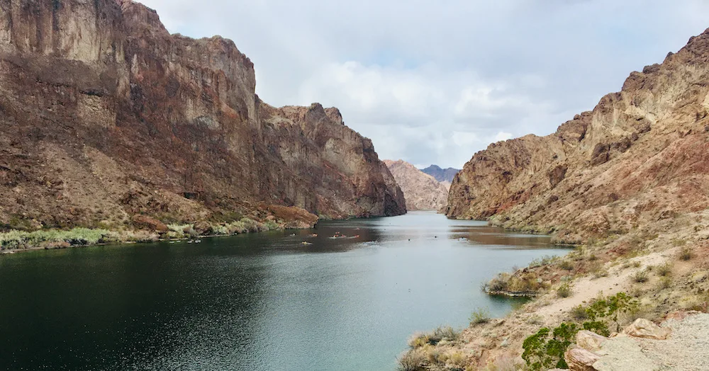 a view of kayakers making their way down the colorado river between rusty mountain walls