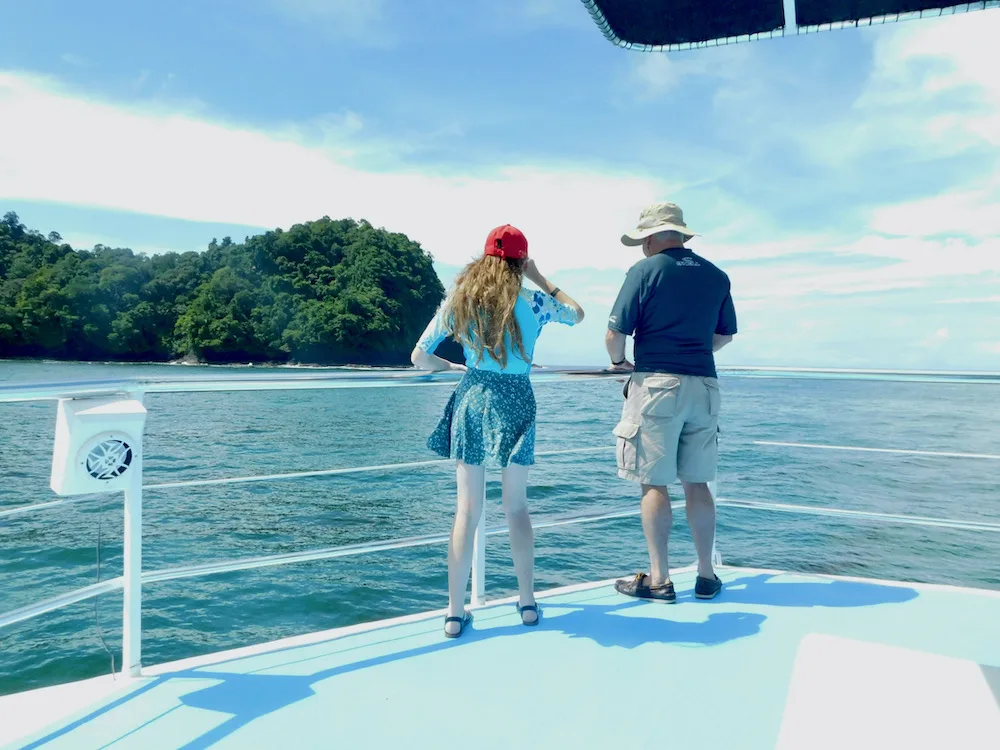 a dad and daughter look for whales over the prow of a catamaran in the shores off of manuel antonio national park.