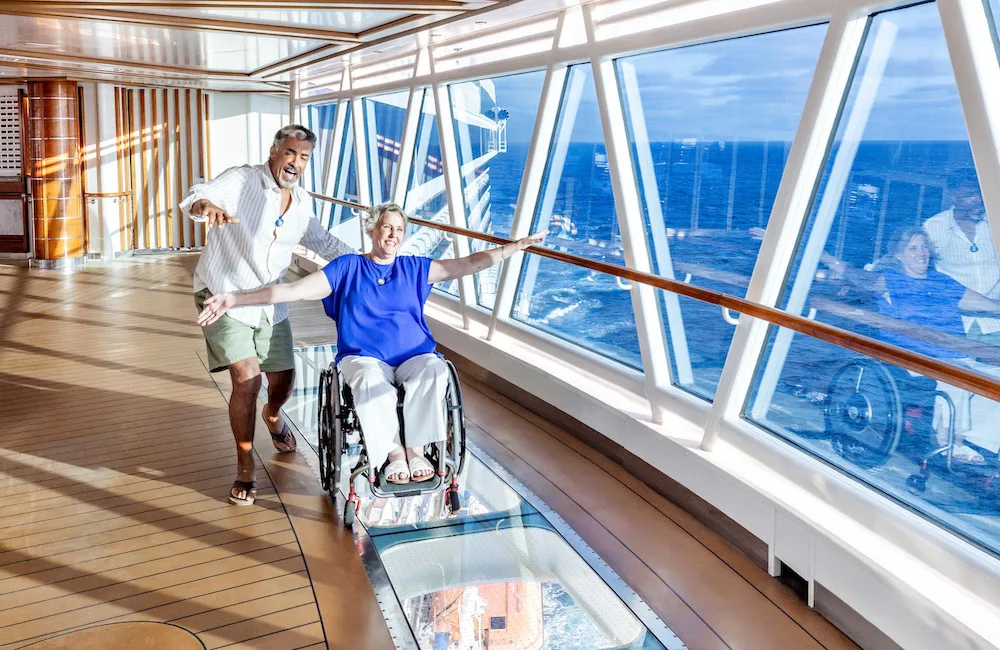 a man and a woman in a wheelchair enjoy a stroll on a princess cruise ship skywalk