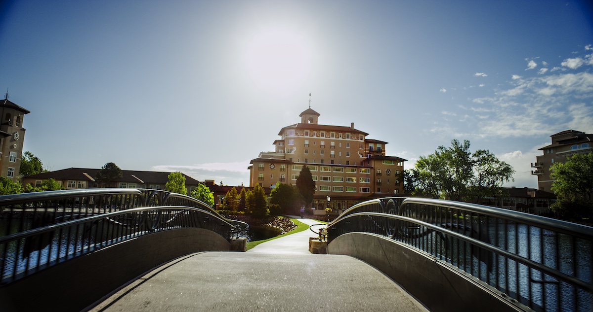 a small pedestrian bridge and winding path leas tothe broadmoor hotel in the rocky mountains. a weekend away here is a mother's day getaway any mom would love.