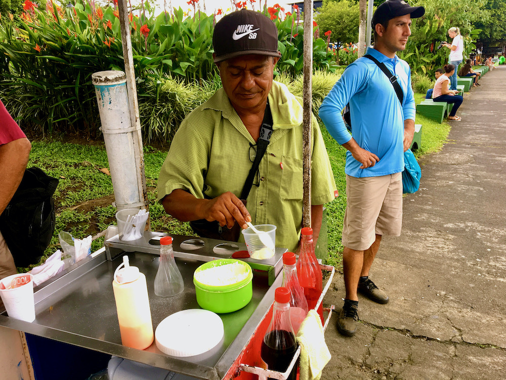 A street cart vendor adds powdered milk to a cup as the base for a granizada in the square in la fortuna cr