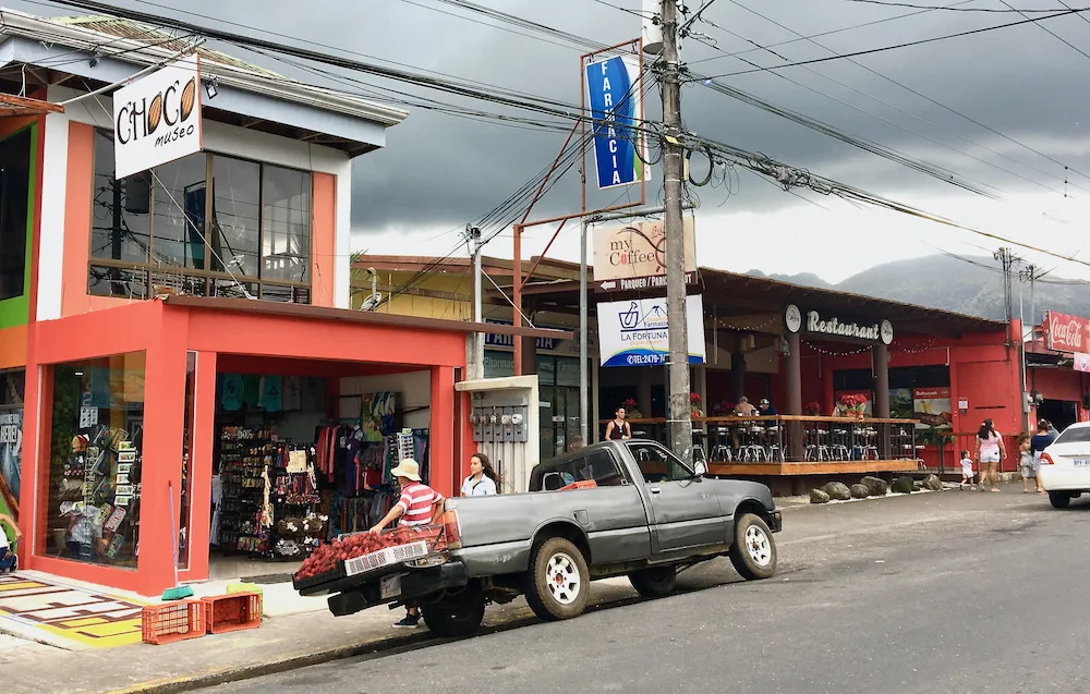 a street in la fortuna, cr with a souvenir shop, restaurants and a man selling rambutans from a truck