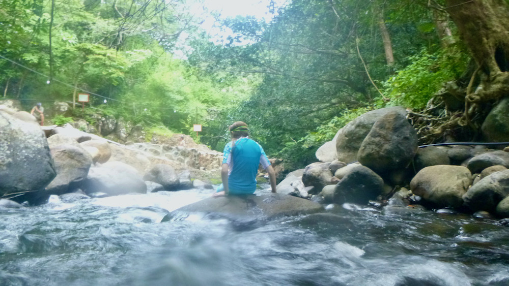 A girl site on a rock amid small rapids in a costa rica river.