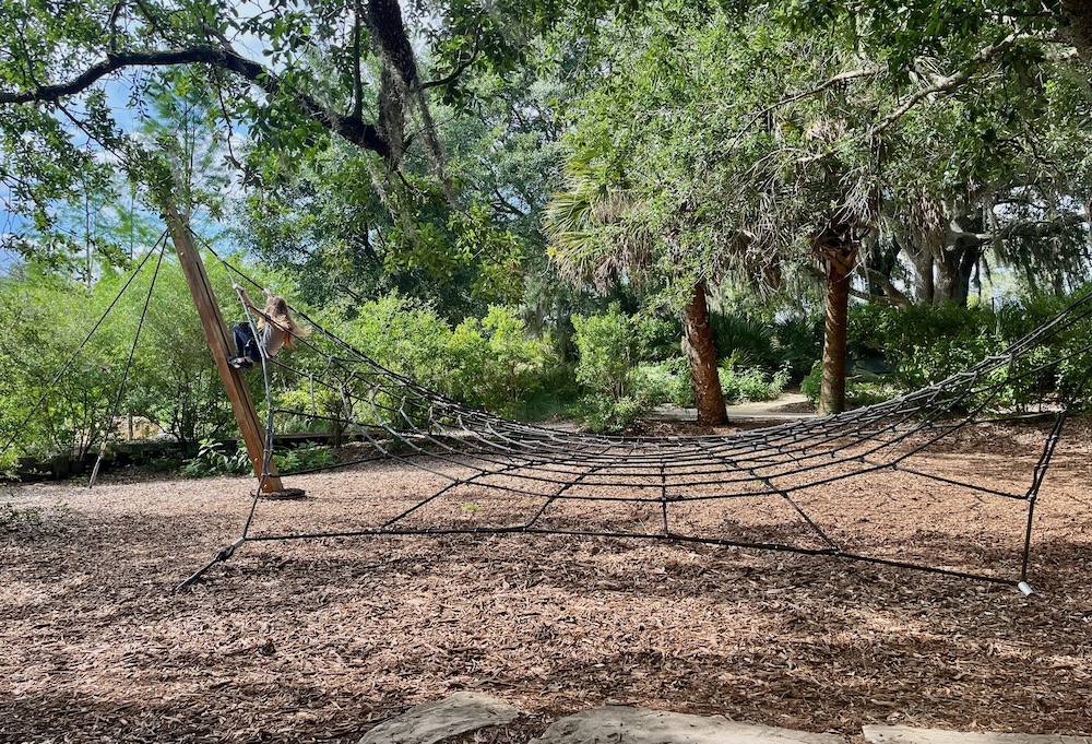 A teen climbs a giant spider web in the hammock hollow kids area at bok tower gardens in central floria