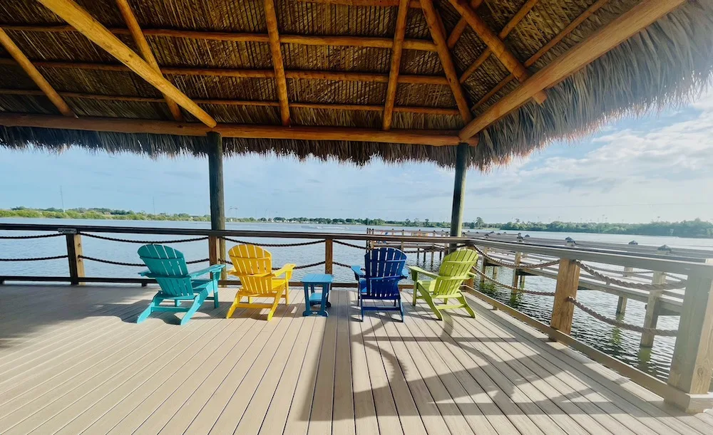 a palm-covered dock with colorful adirondack chairts overlooking a lake is an excellent place to sip an afternoon boat drink at florida's camp margaritaville.