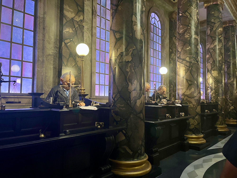 Details at gringotts bank in diagon alley at universal studios include high ceilings, arched windows, marble columns and goblin clerks hard at work.